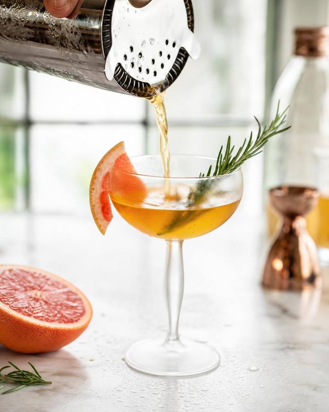 Craft cocktail poured into a chilled coupe with grapefruit and rosemary
